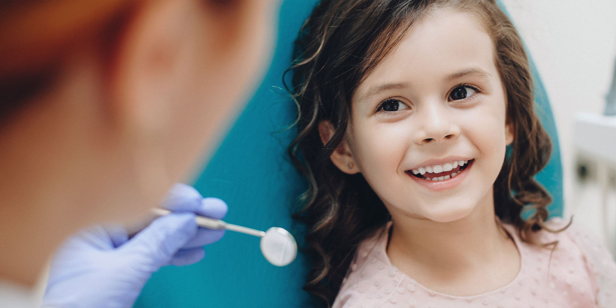 Curly haired little girl looking and smiling to the dentist after a checking up